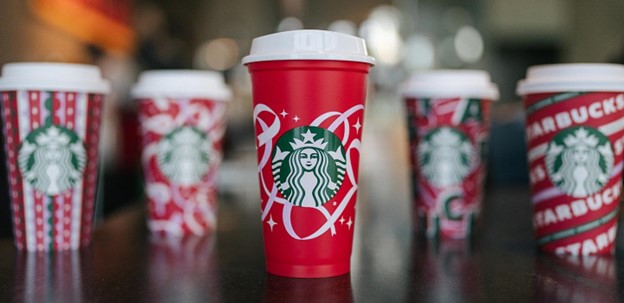 Image of Starbucks holiday cups from previous years with cheery red, green and white designs.